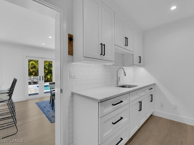 kitchen with sink, white cabinets, decorative backsplash, light stone countertops, and light wood-type flooring