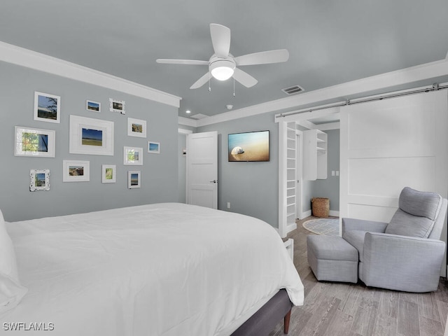 bedroom featuring crown molding, a barn door, ceiling fan, and light wood-type flooring