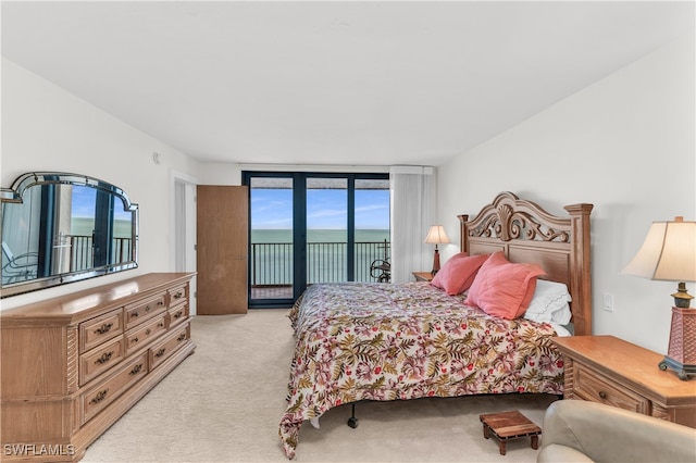 bedroom with access to exterior, light colored carpet, expansive windows, and a water view