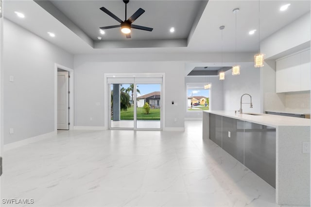 kitchen featuring pendant lighting, a raised ceiling, sink, ceiling fan, and white cabinetry