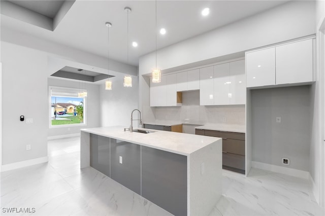 kitchen featuring sink, hanging light fixtures, tasteful backsplash, an island with sink, and white cabinets