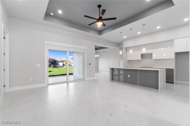 unfurnished living room with a tray ceiling, ceiling fan, and sink