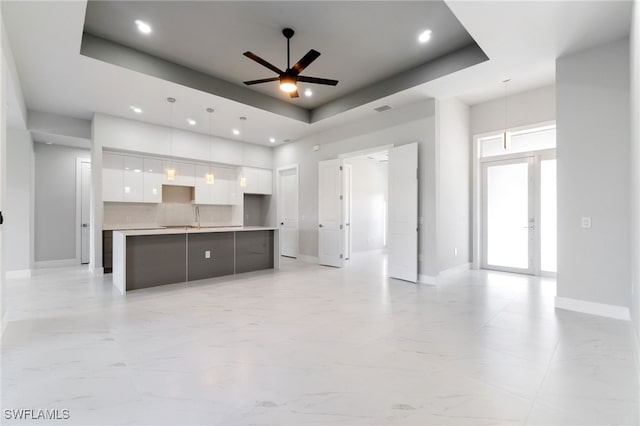 kitchen with a kitchen island with sink, white cabinets, a raised ceiling, hanging light fixtures, and ceiling fan