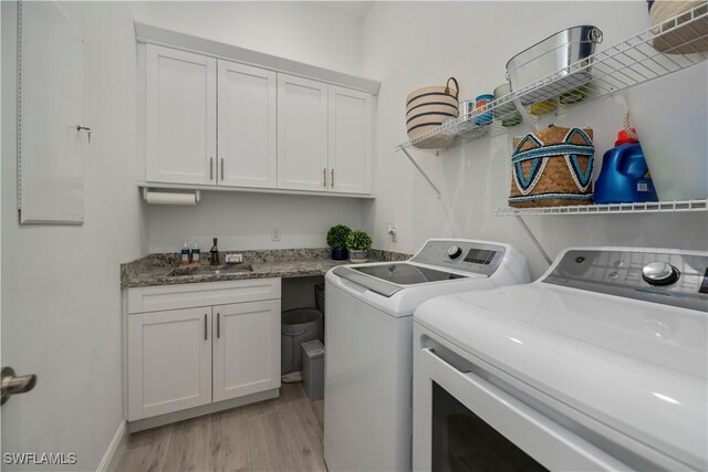 washroom featuring cabinet space, a sink, separate washer and dryer, light wood-type flooring, and baseboards