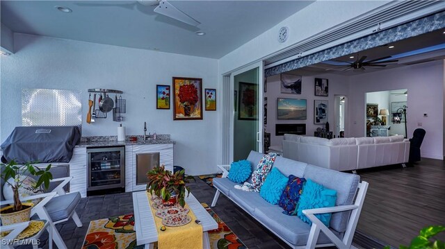 living area featuring beverage cooler, wet bar, ceiling fan, and wood finished floors