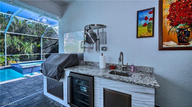 view of patio with wine cooler, an outdoor kitchen, glass enclosure, a sink, and a grill