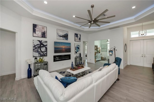 living area featuring ceiling fan, a tray ceiling, light wood-style flooring, and crown molding