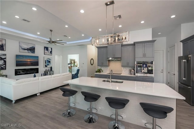 kitchen with a tray ceiling, appliances with stainless steel finishes, a kitchen breakfast bar, open floor plan, and backsplash