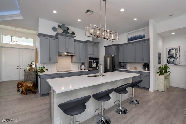 kitchen featuring black electric stovetop, high quality fridge, under cabinet range hood, a sink, and visible vents