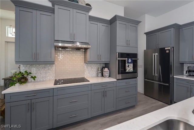 kitchen with under cabinet range hood, light countertops, gray cabinets, appliances with stainless steel finishes, and wood finished floors