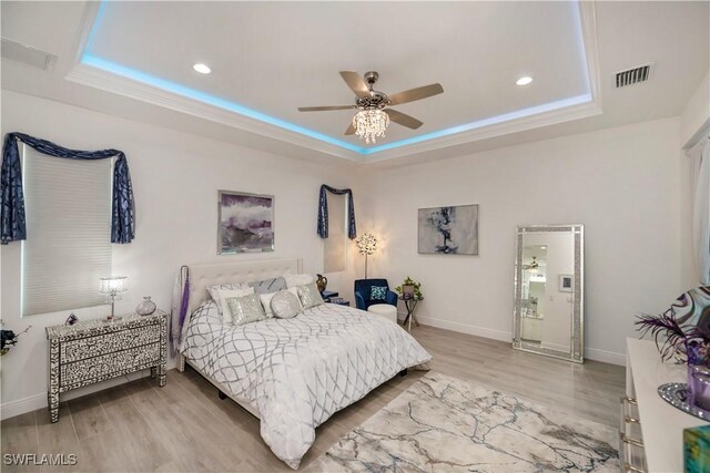 bedroom featuring baseboards, a tray ceiling, visible vents, and light wood-style floors