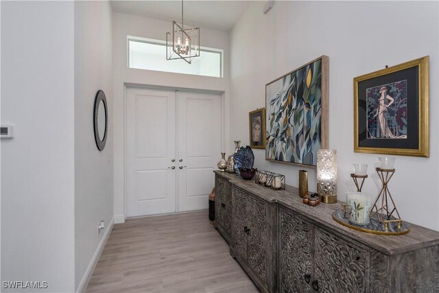 entryway with light wood-type flooring, a high ceiling, baseboards, and an inviting chandelier