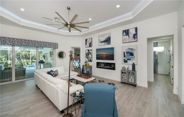 living room with a glass covered fireplace, light wood-style flooring, a raised ceiling, and crown molding