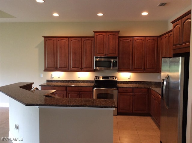 kitchen featuring appliances with stainless steel finishes, light tile patterned floors, and dark stone countertops