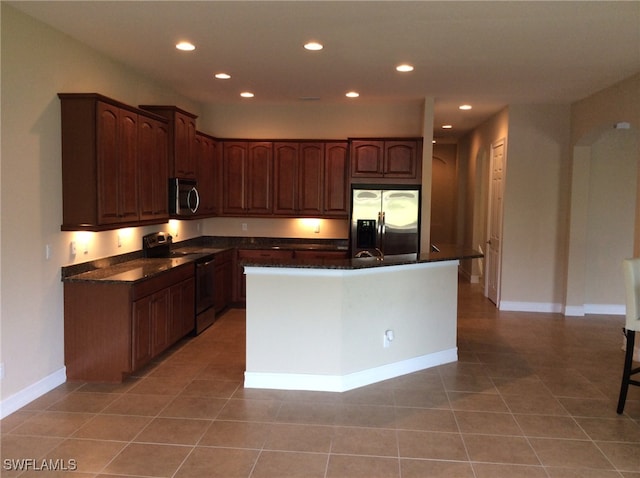 kitchen with appliances with stainless steel finishes, light tile patterned flooring, a center island, and dark stone countertops