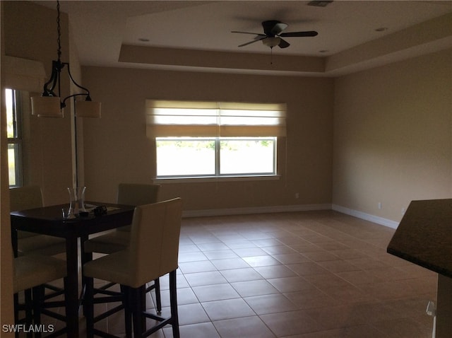 unfurnished dining area featuring ceiling fan with notable chandelier, tile patterned flooring, and a raised ceiling