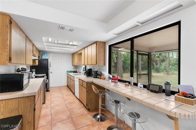 kitchen with electric range, black microwave, tile counters, dishwasher, and light tile patterned floors