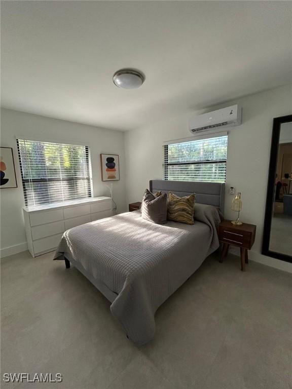 bedroom featuring a wall mounted air conditioner, light carpet, and baseboards