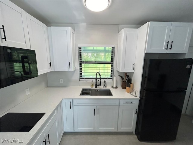 kitchen with a sink, black appliances, white cabinets, and light countertops