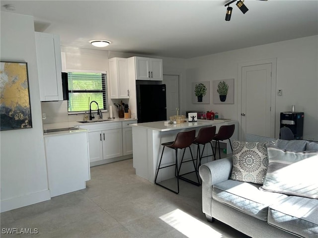 kitchen featuring black refrigerator, a sink, a kitchen breakfast bar, and white cabinetry