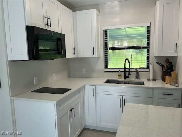 kitchen featuring black appliances, a sink, white cabinetry, light stone counters, and decorative backsplash