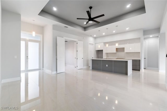 kitchen featuring a tray ceiling, pendant lighting, white cabinets, and a spacious island