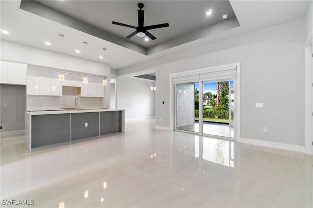 unfurnished living room with a raised ceiling, ceiling fan, and sink