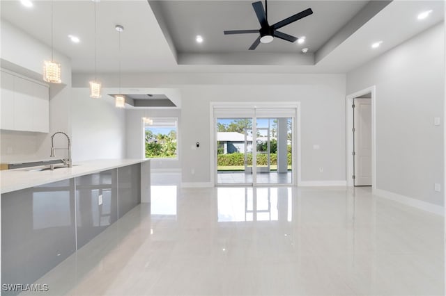 unfurnished living room featuring ceiling fan, sink, and a tray ceiling