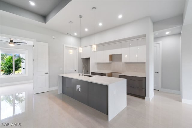 kitchen with ceiling fan, sink, an island with sink, pendant lighting, and white cabinets