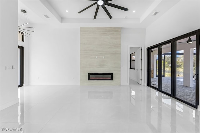 unfurnished living room with a large fireplace, light tile patterned floors, a towering ceiling, and a tray ceiling