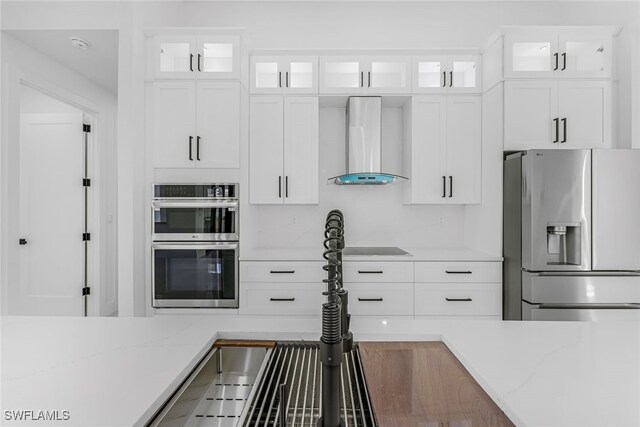 kitchen featuring wall chimney range hood, appliances with stainless steel finishes, glass insert cabinets, and white cabinets