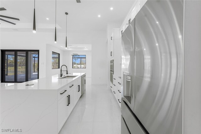 kitchen featuring a sink, white cabinetry, appliances with stainless steel finishes, light stone countertops, and pendant lighting