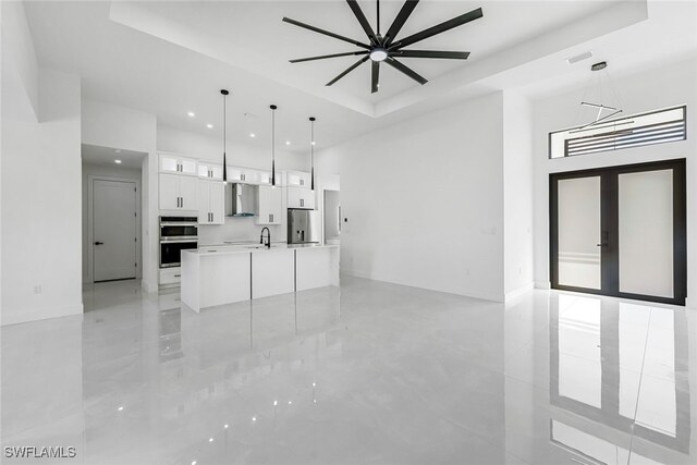 unfurnished living room with a ceiling fan, visible vents, a tray ceiling, and a sink