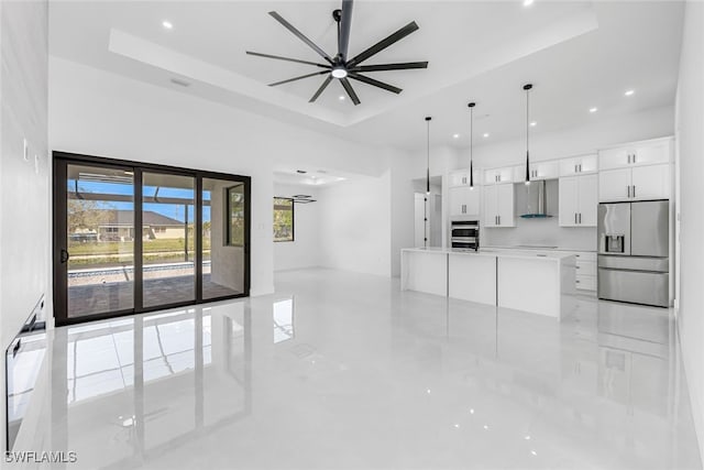 kitchen with stainless steel fridge, a tray ceiling, a spacious island, decorative light fixtures, and white cabinets