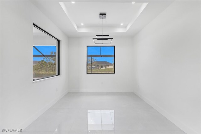 spare room with baseboards, a raised ceiling, and recessed lighting