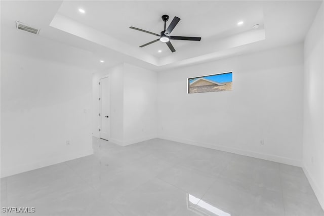 empty room with ceiling fan and a tray ceiling