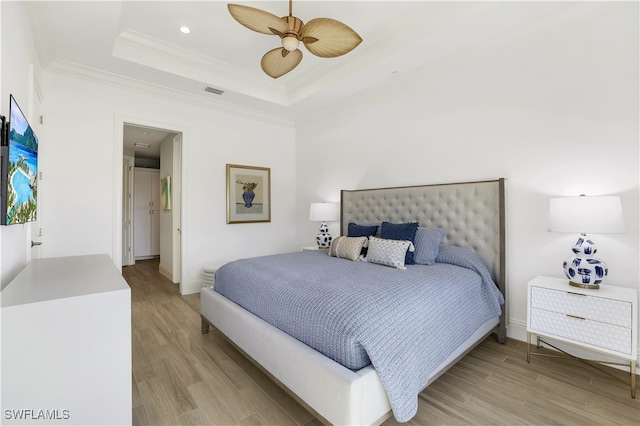 bedroom featuring light wood-type flooring, ceiling fan, crown molding, and a tray ceiling