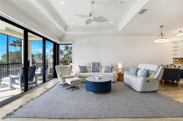 living room with light hardwood / wood-style floors, ceiling fan, crown molding, and a tray ceiling