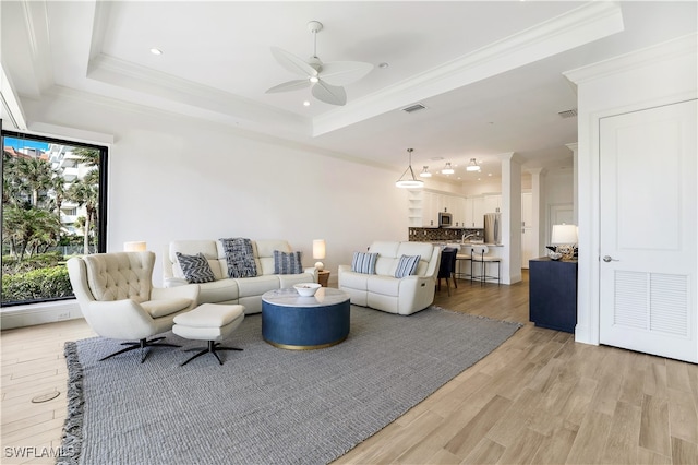 living room with crown molding, light hardwood / wood-style floors, ceiling fan, and a raised ceiling