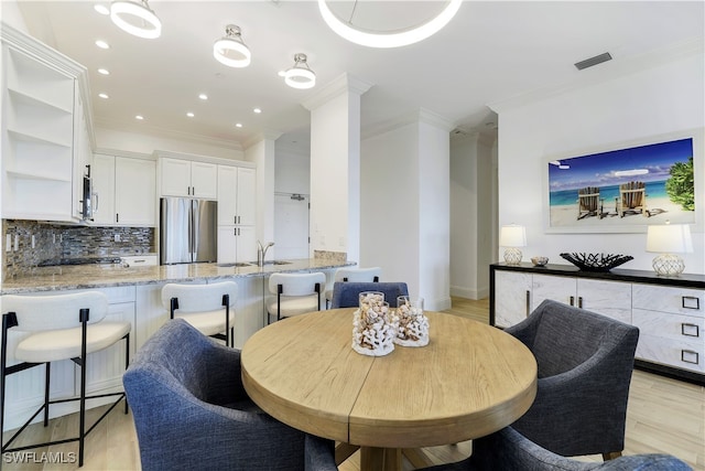 dining space with sink, ornamental molding, and light hardwood / wood-style flooring