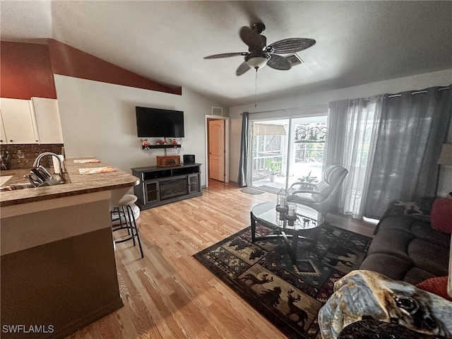 living room with light hardwood / wood-style floors, ceiling fan, sink, and vaulted ceiling