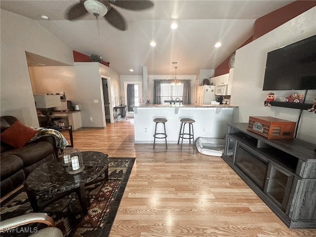 living room with vaulted ceiling, ceiling fan with notable chandelier, and light hardwood / wood-style flooring