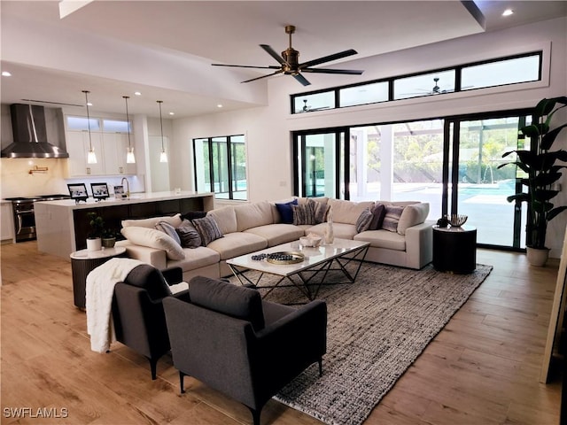 living room with sink, a high ceiling, ceiling fan, and light wood-type flooring