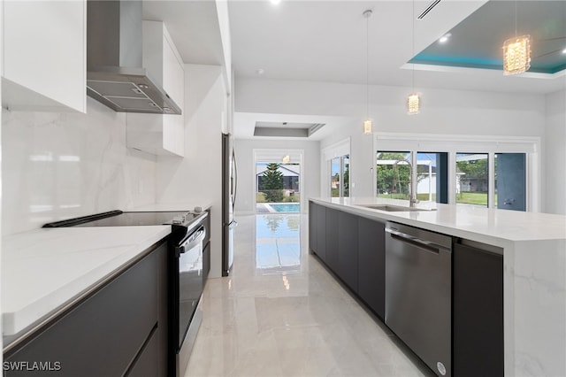 kitchen featuring white cabinets, wall chimney range hood, sink, hanging light fixtures, and stainless steel appliances