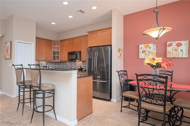 kitchen featuring pendant lighting, light tile patterned floors, a breakfast bar area, stainless steel refrigerator, and decorative backsplash