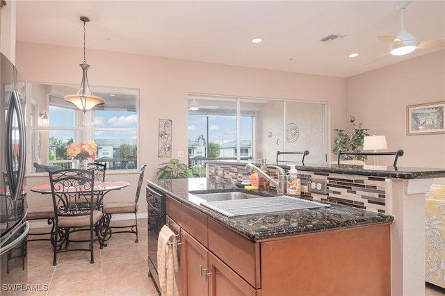 kitchen featuring a center island with sink, stainless steel refrigerator, pendant lighting, dark stone counters, and backsplash