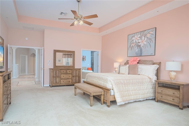 carpeted bedroom featuring a tray ceiling, ensuite bath, and ceiling fan