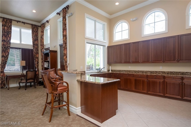 kitchen featuring a towering ceiling, a breakfast bar, light stone counters, kitchen peninsula, and crown molding