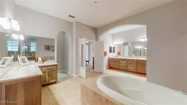 bathroom with tiled tub, vanity, and tile patterned flooring