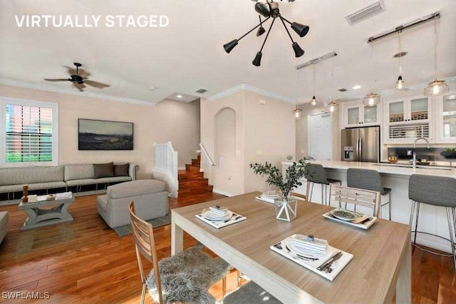 dining space with crown molding, dark hardwood / wood-style flooring, sink, and ceiling fan with notable chandelier